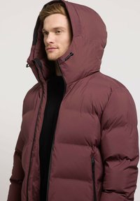 Maroon puffer jacket with a large hood, zippered front, and side pockets. The fabric appears smooth and insulated with a modern design.