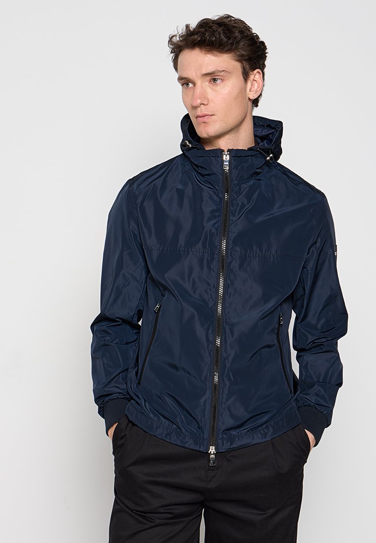 Marineblaues, leichtes Jacket aus glänzendem Material, mit hohem Kragen, Frontreißverschluss und elastischen Bündchen sowie zwei Seitentaschen.