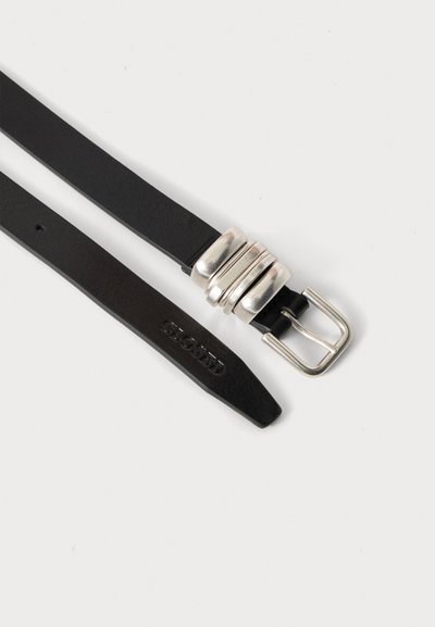 Ceinture en cuir noir avec boucle argentée et trois anneaux argentés, avec le texte embossé « CLOSED » près de l'extrémité pointue.