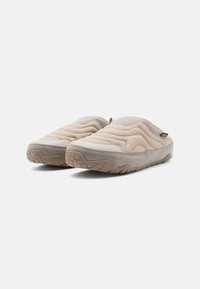 Beige slip-on tøfler med quiltet overdel, grå accenter og gummisål. Har en struktureret overflade og blød, polstret design for komfort.