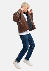 Braune Lederjacke mit strukturiertem Finish, Reißverschlusstaschen und schwarzem Innenfutter. Getragen über einem weißen T-Shirt und blauen Jeans.