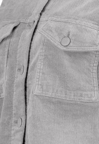 Camicia in corduroy grigio caratterizzata da una texture a coste verticali, chiusura a bottoni e una tasca sul petto con un dettaglio a bottone arrotondato e in rilievo.