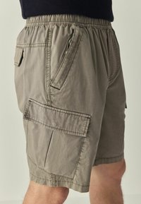 Könnyű szövetből készült khaki rövidnadrág, rugalmas derékkal, oldalsó és rakomány zsebekkel, valamintvarrott részletekkel.