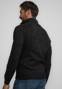 Donkergrijze gebreide sweater met geribbelde kraag en zijdetails, voorzien van een gestructureerd patroon en een aansluitend ontwerp, gedragen over blauwe spijkerbroek.