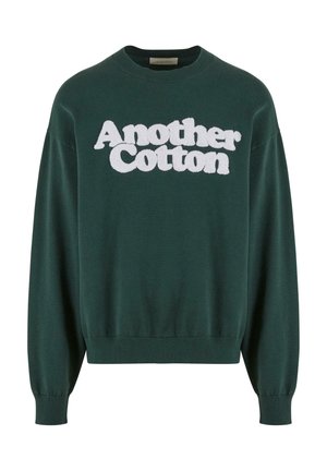 Roheline puuvillane dressipluus, millel on valge, koheva kirjatükiga tekst "Another Cotton", ümmargune kaelus ja soonikkoes varrukad ja alläär.