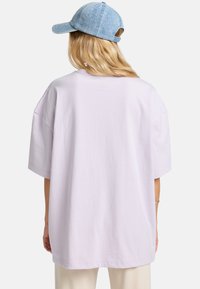 Camiseta de algodón lavanda de gran tamaño con mangas cortas, llevada al revés. Combinada con una gorra de denim azul claro para un look casual.