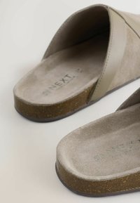 Pelēkas zamšādas iešļūcenes ar gludu virsmu, kurām ir gaiši pelēks siksniņa, korķa līdzīga zole un reljefa zīmola nosaukums uz zolītes.