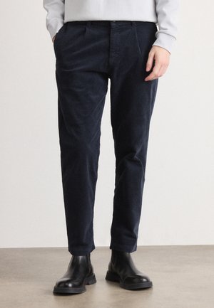 Pantalones de pana en color azul marino con un diseño de pierna recta, que presentan una textura sutil y bolsillos laterales, combinados con botines negros.