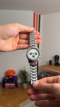 Silberne Edelstahl-Uhr mit einem runden weißen Zifferblatt, blauen Unterziffern und silbernen Gliedern am Armreifen, ausgestattet mit minimalistischen Stundenmarkierungen.