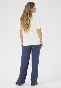 T-shirt en mélange de coton de couleur crème clair, associé à un pantalon large bleu marine en tissu texturé avec des poches latérales. Les chaussures présentent un imprimé animal.