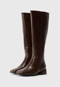 Ein Paar hohe, dunkelbraune Lederstiefel mit niedrigen Blockabsätzen, runden Zehen und sichtbarem Nähen auf einem schlichten weißen Hintergrund.