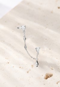 Srebrny pierścień z łańcuszkiem łączącym dwa łezkowate przezroczyste kamienie, z teksturowaną powierzchnią i misternymi detalami.