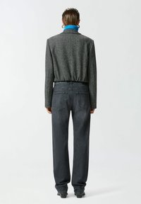 Sivi vuneni sako s krojenim strukom, uparen s tamnoplave traperice viskog struka. Plavi detalj na ovratniku vidljiv je na vratu.