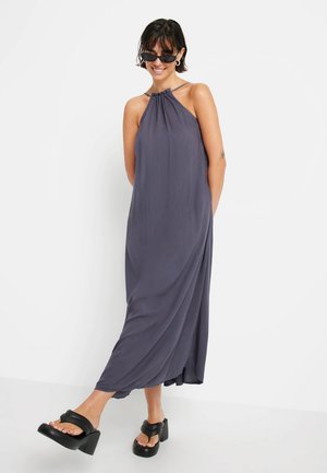 Abito maxi in tessuto grigio scuro, con collo all'americana, design drappeggiato e silhouette fluida. Abbinato a sandali platform neri e spessi.