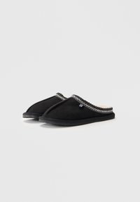 Svarta slip-on-tofflor i mjuk mocka, med en texturerad övre kant med sicksackstygn och en gummisula för hållbarhet.
