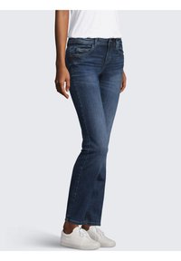 Jean en denim avec une taille mi-haute, couleur bleu foncé, léger délavage et coupe droite, associés à des baskets blanches.