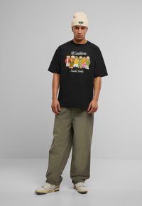 Svart bomulls T-skjorte med et grafisk trykk av tegneserie-beringer i forskjellige antrekk. Kombinert med løse olivengrønne bukser og kremfargede sneakers. Beige beanie.