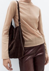 Beige langærmet bluse med en subtil tekstur, parret med en mørkebrun ruskinds skuldertaske med en aftagelig rem. Brune læderbukser.