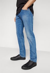 Világoskék denim farmer egyenes szárú szabással, elülső zsebekkel és enyhe kopással. Fekete sportcipővel párosítva.