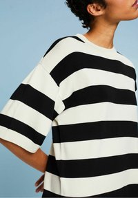 Personne portant un t-shirt à manches courtes à larges rayures horizontales noires et blanches sur fond bleu clair.