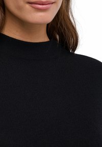 Czarny prążkowany sweter z wysokim kołnierzem, teksturowaną tkaniną i subtelnymi detalami przeszyć, widoczny powyżej klatki piersiowej.