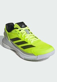 Chaussure de course jaune néon vif avec des rayures noires, semelle grise, col rembourré noir et lacets jaunes, inclinée pour montrer le côté et le dessus.