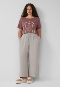 Losse mauve graphic tee met witte tekst en ontwerp, gecombineerd met lichtgrijze wijde broek met elastische tailleband en zakken.
