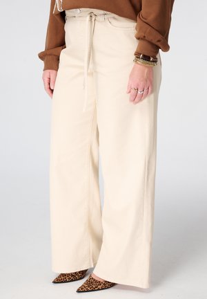 Pantalon crème à jambes larges avec taille à cordon, associé à des chaussures pointues imprimé léopard et un haut marron à manches longues.