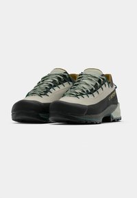 Zapatos de exterior ligeros en gris y negro, con una resistente cubierta de goma en la puntera, suela texturizada y cordones en verde y dorado.