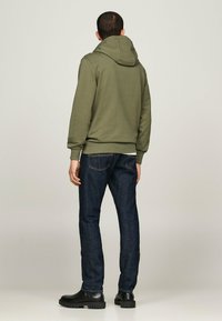 Felpa verde oliva con cappuccio, polsini e orlo a coste. Indossata con jeans blu scuri e stivali neri alla caviglia con suola testurizzata.