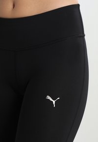 Mustat liikuntaleggingsit, jotka on valmistettu joustavasta materiaalista, jolla on sileä pinta. Lankaan on ommeltu pieni hopeinen Puma-logo reiteen.