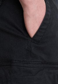 Black fabric with a smooth texture, featuring a horizontal pocket cutout at the side, stitched seams, and a simple, functional design.