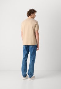 Beige kortærmet t-shirt parret med blå denim jeans. T-shirten har et simpelt design, og jeansene har en lige pasform.