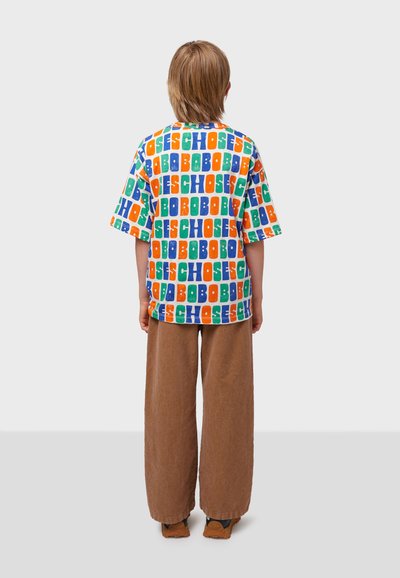 Colorful short-sleeve shirt with a geometric letter print in orange, blue, green, and red. Paired with loose, brown corduroy pants.
