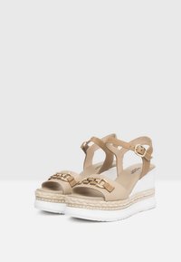 Sandali platform beige con cinturini alla caviglia, dettagli in hardware dorato, suola in espadrille texturizzata e materiale sintetico liscio.