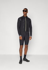 Veste de cyclisme noire avec des zips contrastants, accompagnée de shorts noirs. Présente un design élégant, un tissu extensible et une silhouette ajustée.