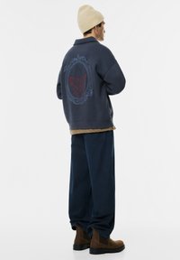 Mørkeblå oversize sweatshirt med et rødt og blåt grafik på ryggen, parret med mørke denimbukser og brune ankelstøvler.