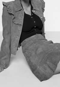 Gray suede jacket with ruffled details, paired with a fitted black ribbed top and a matching gray suede skirt. Smooth texture throughout.