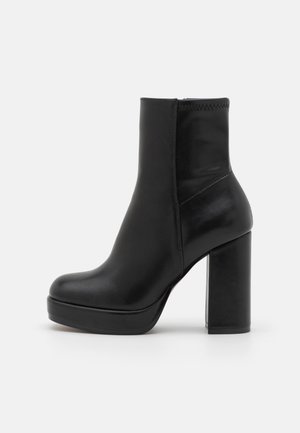 Bottine en cuir noir avec bout arrondi, semelle plateforme et talon bloc haut et épais, montrée de profil sur fond blanc.