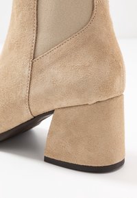 Bottines en daim tan avec un talon carré, présentant une texture lisse et des panneaux latéraux élastiques pour un enfilage facile.
