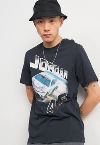 Camiseta de algodón negra con un gráfico de un coche de carreras, texto "JORDAN 45" en negrita blanca y gris, mangas cortas, corte relajado.