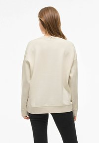 Beige sweatshirt med avslappnad passform, långa ärmar och ribbade manschetter. Mjuk textur, rundad halsringning och en något längre bakham.