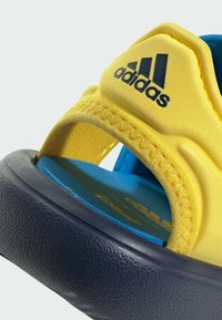 Adidas sandals featuring a yellow synthetic upper, navy rubber sole, textured finish, and blue interior with logo detail.
