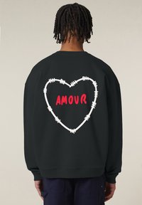 Felpa nera a vestibilità ampia. Presenta un design a forma di cuore realizzato con filo spinato bianco e la parola "AMOUR" in lettere rosse sulla schiena.