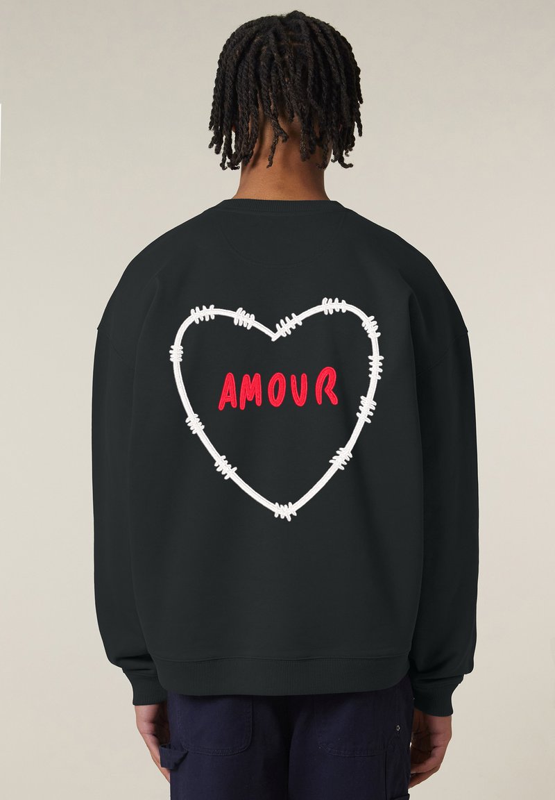 Felpa nera a vestibilità ampia. Presenta un design a forma di cuore realizzato con filo spinato bianco e la parola "AMOUR" in lettere rosse sulla schiena.