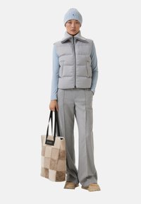 Grå puffervest med høj krave, blå langærmet top, grå ternede flared bukser og en fluffy patchwork tote taske med sorte håndtag.