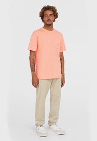 Lyse orange kortærmet t-shirt med en brystlomme og et lille logo. Sættes sammen med beige bukser og hvide sneakers.