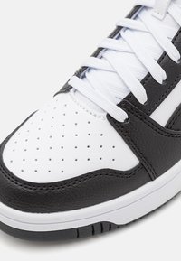 Zwart-witte sport sneakers met een textured leren bovenkant, geperforeerde witte neus en platte witte veters, met een rubberen zool.