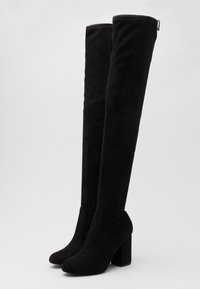 Bottes noires au-dessus du genou en daim doux avec un talon bloc. Texture lisse et lignes épurées, avec un bout arrondi et sans éléments métalliques visibles.