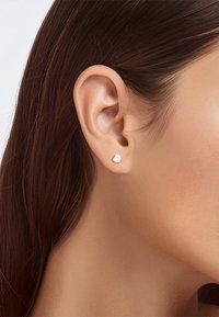 Goujon en argent, forme ronde, finition polie, posé dans une oreille percée. Texture lisse, design minimaliste, dessiné sur la peau.